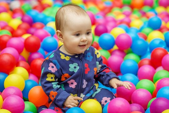 Baby sitting in colorful ball pit reaching for balls