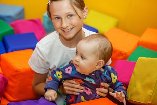 Older sister carrying baby girl in indoor soft play area