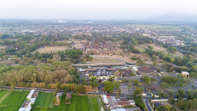 Aerial view of Prambanan Temple surrounded by lush green rice fields, ancient stone structures, and local vegetation in Kecamatan Prambanan, Daerah Istimewa Yogya, Indonesia.