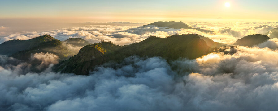 Aerial view of Dieng Plateau mountain peaks rising above a sea of clouds at sunrise in Indonesia.