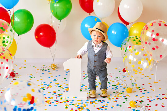 Happy one-year-old boy celebrating his first birthday with a colorful cake, bright balloons and vibrant party decorations.
