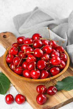 Fresh ripe sweet cherries in rustic wooden bowl with green leaves on light textured background. Top view flat lay with copy space. Juicy organic summer fruit, red berries, healthy seasonal food