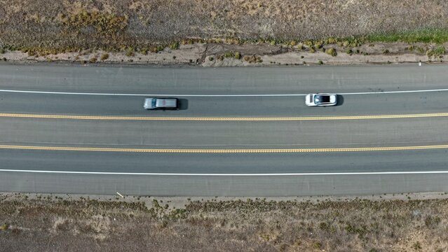 Aerial view of two cars driving on a multi-lane highway surrounded by dry grassy fields in Golden, Colorado, United States.