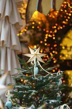 Christmas tree decorated with white star, ornaments and warm fairy lights, displayed outdoors with festive illuminated, light bokeh background and snowy branches. Holiday atmosphere, aesthetic mood