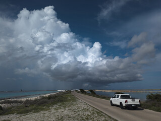 White pickup truck driving on coastal road under dramatic storm clouds in Bonaire © zimagine