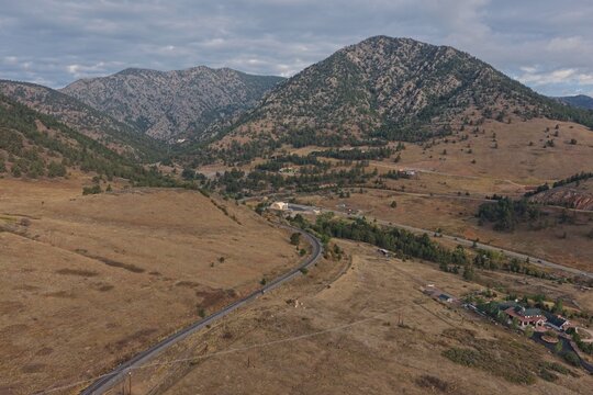 Aerial view of the mountainous landscape near Golden, featuring a winding road, dry grassy hills, pine trees, and a small building complex in Golden, Colorado, United States.