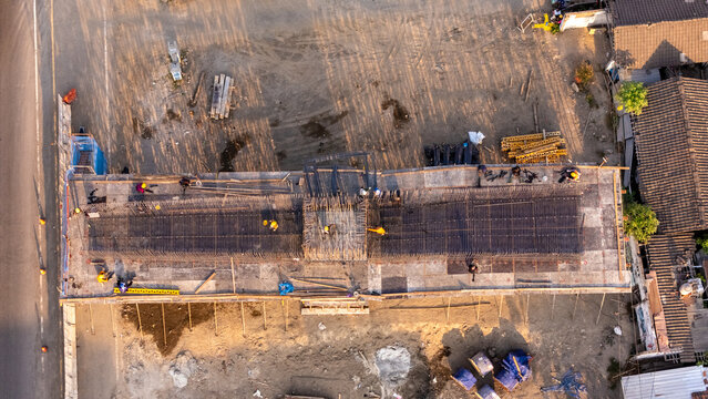 Aerial view of construction workers installing steel rebar framework for a building foundation at a construction site in Indonesia.