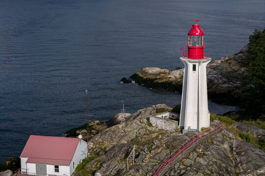Aerial view of the historic lighthouse at Lighthouse Park, featuring a white tower with a red lantern room on rocky coastal terrain in West Vancouver, British Columbia, Canada.
