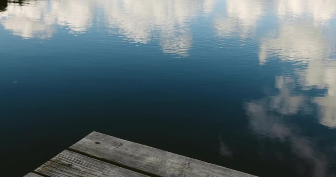 Cinematic autumn lakeside scene with a weathered wooden dock reflected in calm blue water and soft clouds.