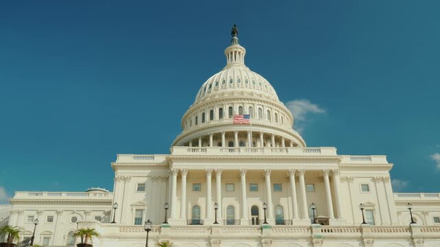 Iconic washington d c landmark united states capitol building with american flag fluttering against clear blue sky in sunny weather.