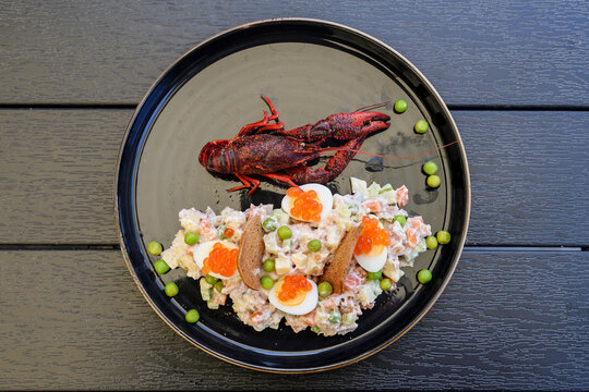 A portion of salad served on a large ceramic platter, accompanied by a whole boiled red crayfish, an exquisite seafood appetizer, top view, close-up.