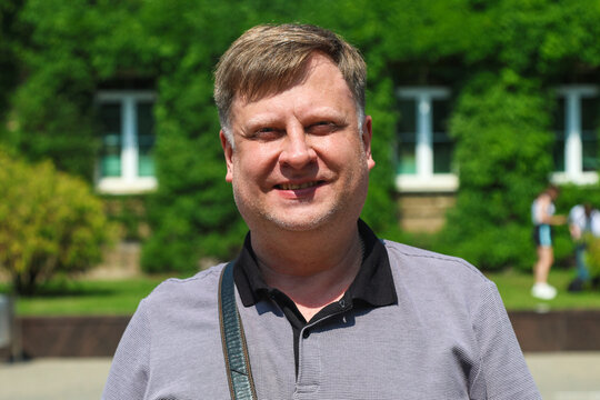 Portrait of an adult European man against a building completely overgrown with lush green ivy plants, blending nature and urban architecture.