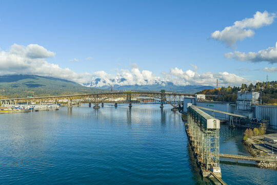 Aerial view of the Ironworkers Memorial Second Narrows Crossing spanning Vancouver Harbour with grain terminals and mountains under a blue sky in Vancouver, British Columbia, Canada.