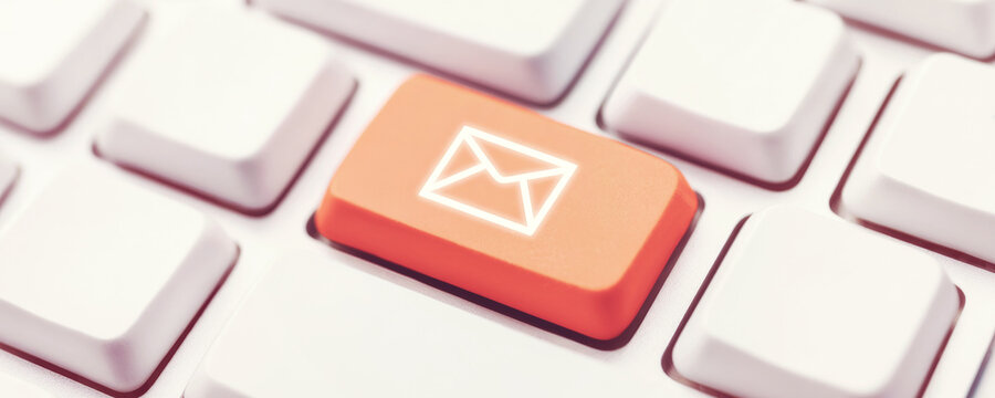 Orange email button on a white computer keyboard representing online communication and digital messaging