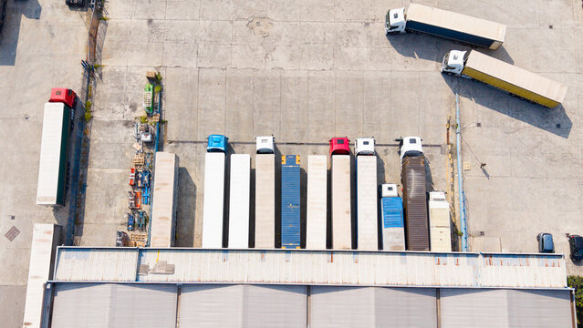 Aerial view of semi-trucks and trailers parked at a distribution center loading dock with concrete yard in San Giuliano Milanese, Lombardy, Italy.