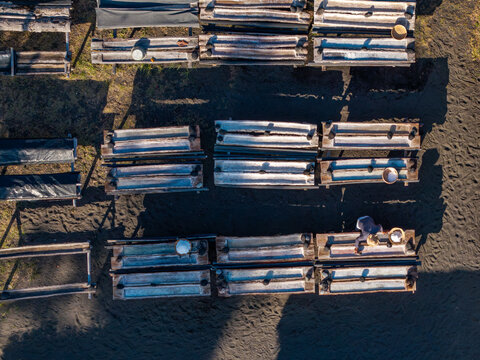 Aerial view of a traditional natural salt maker with wooden troughs filled with salt crystals and a worker harvesting on dark volcanic sand in Kecamatan Dawan, Bali, Indonesia.