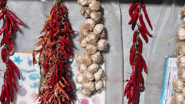 Video showing strings of dried red chili peppers and bundles of garlic displayed at an outdoor market