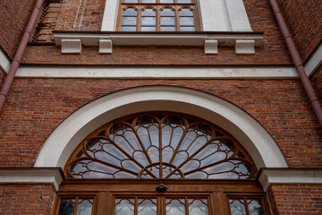 Arched wooden transom window with ornate tracery above entrance on historic red brick building facade, representing classical architecture and restoration. © Marina