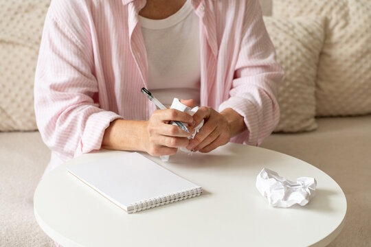 Mature woman crumples sheet of paper while writing at home, notebook and pen lie on table. A quiet domestic activity and an unsuccessful first attempt