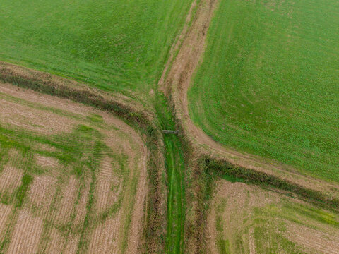 Aerial view of agricultural farmland featuring green fields, freshly harvested brown fields, traditional hedgerows, and dirt tracks in Looe, Cornwall, United Kingdom.