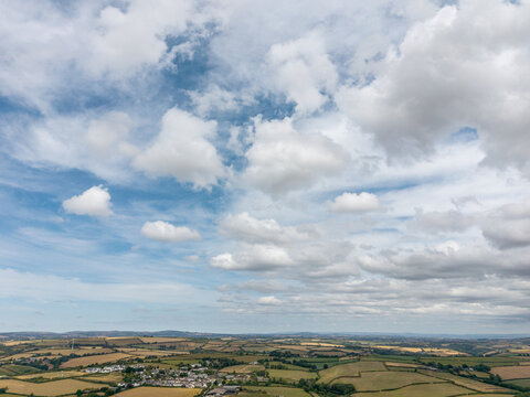 Aerial view of rural landscape featuring patchwork agricultural fields, hedgerows, and rolling hills under a bright sky with scattered clouds in Looe, Cornwall, United Kingdom.
