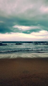 Eye level view of gentle ocean waves crashing on sandy shore under dramatic clouds at My Khe Beach in Da Nang, Vietnam