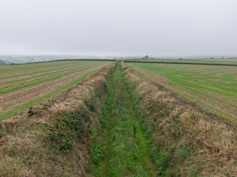 Aerial view of misty rural countryside with agricultural farmland and a narrow country path under a foggy sky in Looe, Cornwall, United Kingdom.