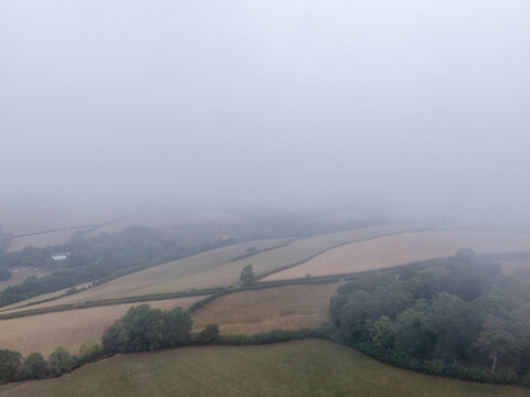 Aerial view of misty rural countryside with foggy agricultural farmland, rolling hills, and country roads in Looe, Cornwall, United Kingdom.
