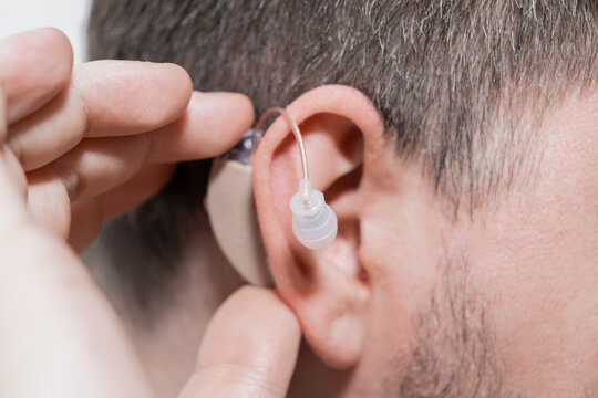 A man adjusting a small discreet hearing aid behind his ear to improve auditory perception and restore clarity in daily communication for a better quality of life and social connection