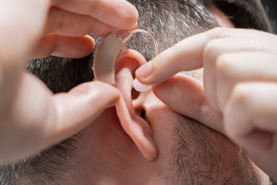 A man fitting a modern beige hearing aid into his ear to improve auditory clarity, depicting personal healthcare assistance and assistive medical technology for daily sound restoration