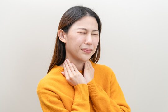 Sore throat in flu season. Young asian woman touching her neck and feeling pain in throat in the bedroom at home.