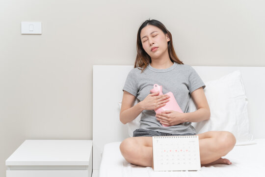 Menstruation symptom concept, Close-up woman touching her belly and feeling stomach pain from cycle period on the bed at home.