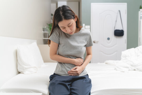 Menstruation symptom concept, Close-up woman touching her belly and feeling stomach pain from cycle period on the bed at home.