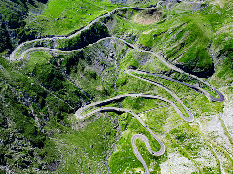 Aerial view of the winding Transfagarasan mountain road with its sharp hairpin turns and steep slopes, surrounded by lush green mountains in Curtea de Arges, Judetul Arges, Romania.