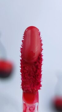 Thick red liquid dripping on the tip of a mini brush. Front close up view for beauty product concept. Isolated on soft white background with cherry decoration. Cosmetic or lip tint application.
