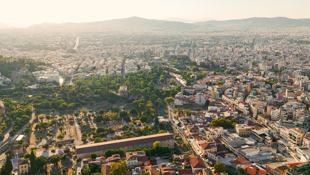 Aerial view of the Temple of Hephaestus surrounded by the lush greenery of the Ancient Agora and the dense urban sprawl of Athens, Greece.