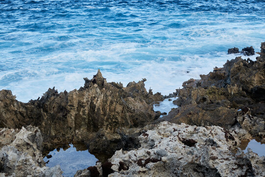 Ocean waves crashing against sharp volcanic coral rock coast