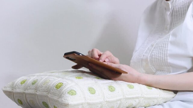 クッションを膝に乗せてくつろいでスマートフォンを操作する人の手元