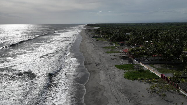 Aerial view of San Marcelino beach featuring dark volcanic sand, rows of palm trees, and ocean waves crashing along the coastline in La Paz Centro, La Paz, El Salvador.