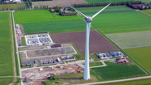 Aerial view of a wind turbine standing in a rural landscape surrounded by agricultural fields and an electrical substation in Espel, Flevoland, Netherlands.