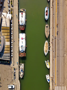 Aerial view of the historic canal in Cervia lined with various boats, including fishing vessels and small yachts, moored along the stone quays in Cervia, Emilia-Romagna, Italy.