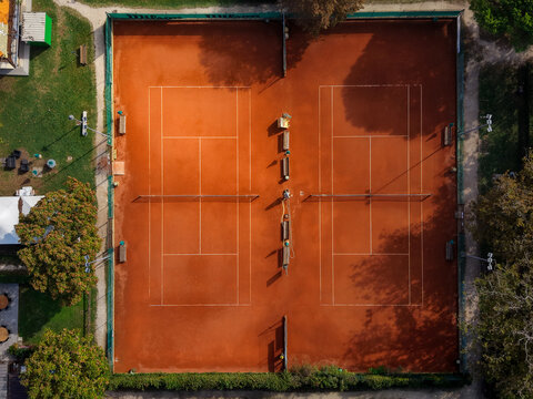 Aerial view of two clay tennis courts surrounded by green trees and park grounds in Cervia, Emilia-Romagna, Italy.