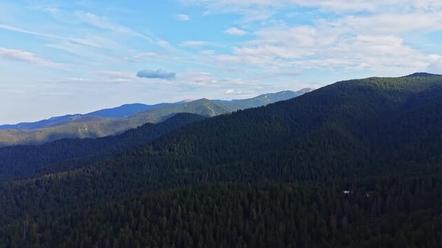 A view of mountains covered with trees and a blue sky. Light clouds are visible, indicating daytime. The scene displays a natural landscape with no signs of human activity.