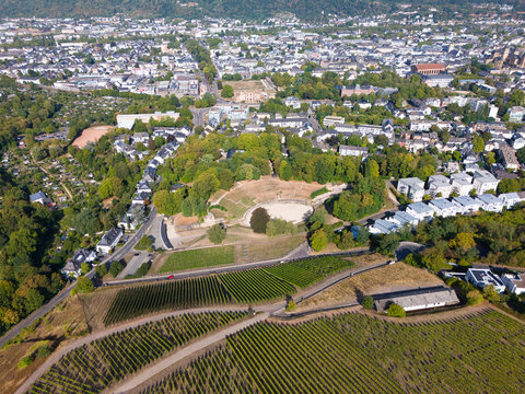 Aerial view of the historic Roman amphitheater in Trier, surrounded by lush vineyards, urban rooftops, and the scenic Moselle river valley in Trier, Rhineland-Palatinate, Germany.