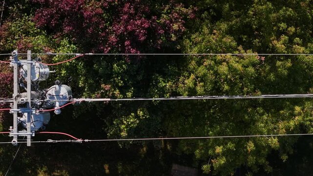 Aerial view of high voltage electrical transformers and power lines over lush green trees.