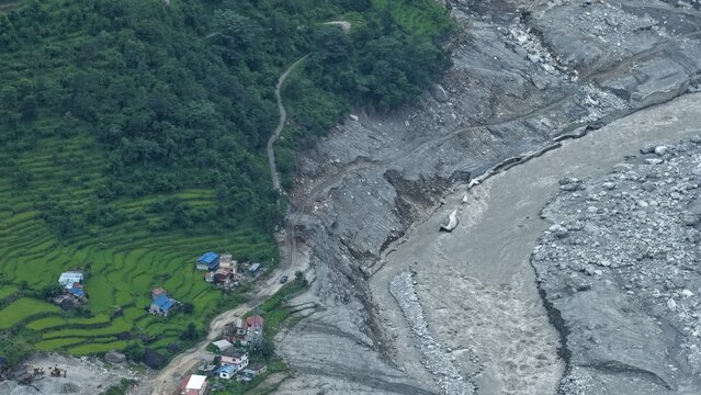 Aerial view of landslide damage along the riverbank, with terraced green fields and small houses in Betrawoti Bazaar, Bagmati Province, Nepal.