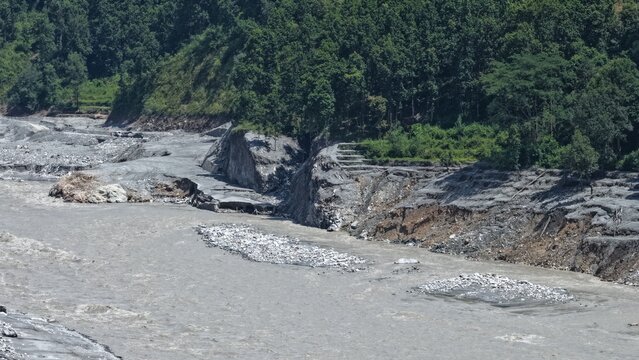 Aerial view of the river flowing through the landscape with rocky riverbanks, sediment deposits, and dense forest in the background in Betrawoti Bazaar, Bagmati Province, Nepal.