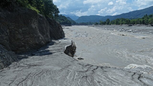 Aerial view of the turbulent, sediment-heavy Trishuli River flowing through a rocky landscape with eroded riverbanks and distant mountains in Betrawoti Bazaar, Bagmati Province, Nepal.