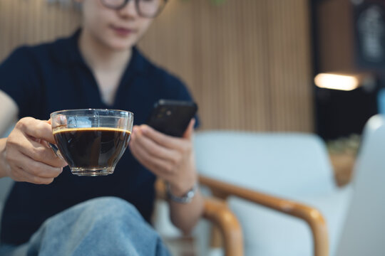 Asian business woman hand holding a cup of black coffee and using smartphone at cafe, modern people lifestyle
