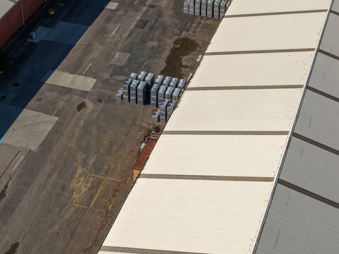 Aerial view of pallets of bricks and pavers stored in an industrial yard next to a large warehouse building in Melbourne, Victoria, Australia.